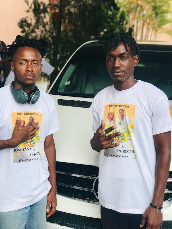 Two men wearing custom wedding-themed t-shirts, posing outdoors with a car backdrop.