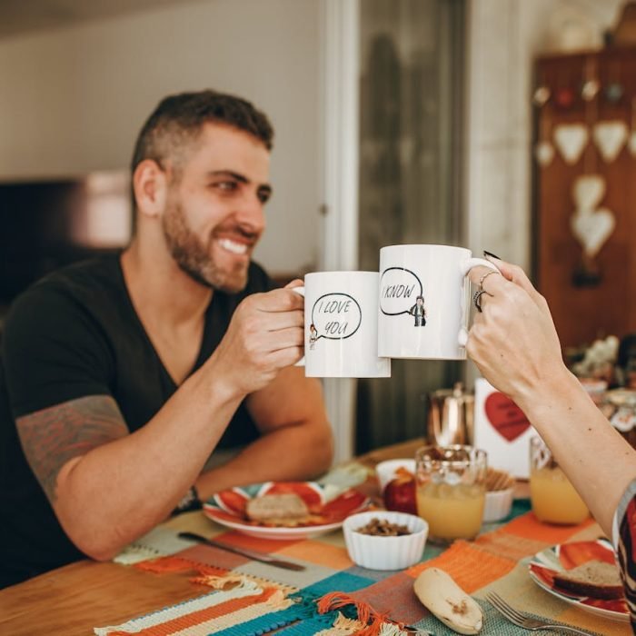A joyful couple toasting with customized mugs during breakfast at home.
