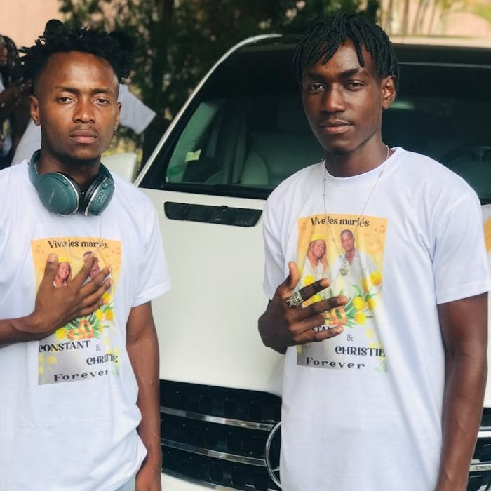 Two men wearing custom wedding-themed t-shirts, posing outdoors with a car backdrop.